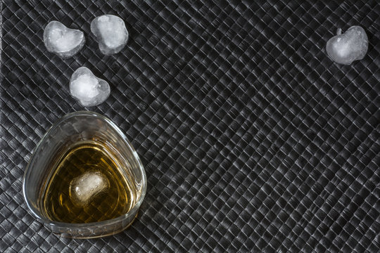 One glass of bourbon with ice on black leather background