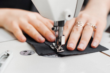 Woman hands with fabric at sewing machine. Seamstress working behind her equipment. Tailoring process, designer workshop, garment industry concept