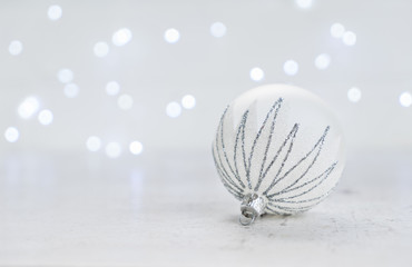 Christmas scene with one white and silver ball and christmas lights in background