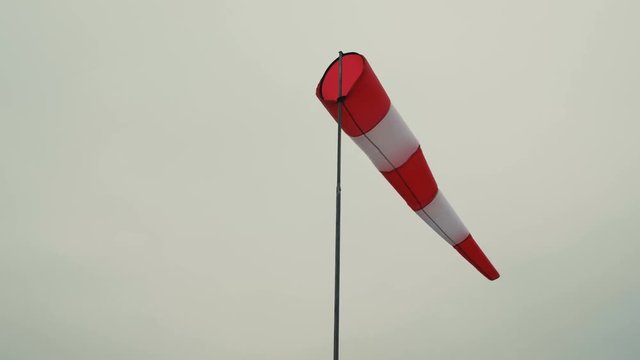 Inflated air sleeve windsock show direction of wind blowing near helicopter landing place site on background of gray sky.