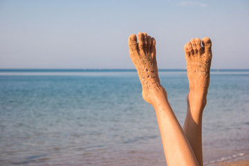 Female legs on sea background. Feet covered in sand. No bustle and problems. Vacation of your...