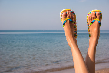 Woman's legs and sea. Feet wearing flip flops. Leave bustle and problems behind. The dream vacation.