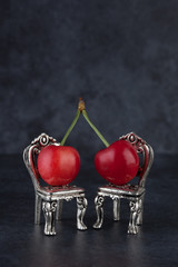 Couple of red cherries placed on beautiful silver vintage chairs on dark background with copy space. Relationship concept, vertical image.