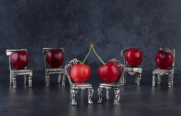 Red delicious ripe cherries on vintage small silver chairs and dark background