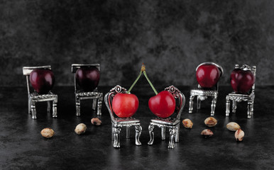Red delicious ripe cherries on vintage small silver chairs  with cherrystones on dark background with copy space