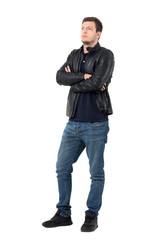 Fototapeta premium Serious young casual man in leather jacket and jeans with crossed arms looking away. Full body length portrait isolated over white studio background.