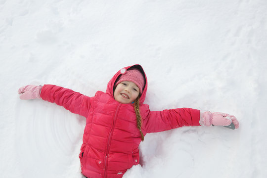 Playful girl playing in snow, making a snow angel
