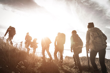 Group of hikers walking on a mountain at sunset - obrazy, fototapety, plakaty