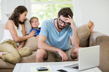Tensed man sitting on sofa with laptop and bills