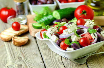 Greek salad with fresh vegetables,feta cheese and olive oil on rustic wooden background.Healthy fresh vegetarian food.Close up.