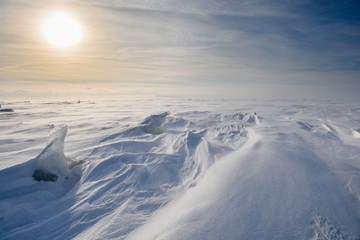 Boundless icy landscape during a snowstorm at sunset in winter.
