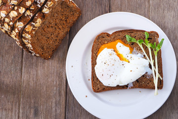 Top view of poached egg on rye bread on a wooden table.