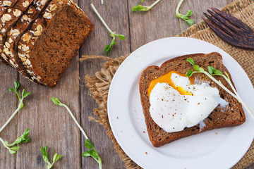 Top view of poached egg on rye bread on a wooden table.