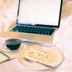 Breakfast in bed with coffee, cake and laptop