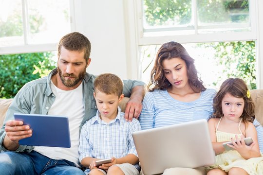 Family sitting on sofa and using a laptop, tablet and phone