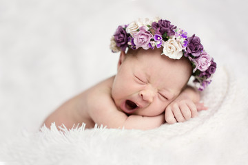 newborn sleeping yawns with wreath of purple flowers on light background, real life,  lifestyle, © natalialeb