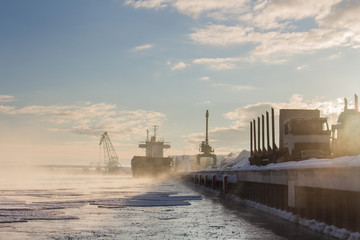 Winter industrial lanscape with trucks and Bulker in a Harbour, loading wood.