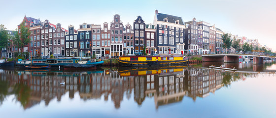 Panorama of Amsterdam canal Singel with typical dutch houses, bridge and houseboats during morning blue hour, Holland, Netherlands.