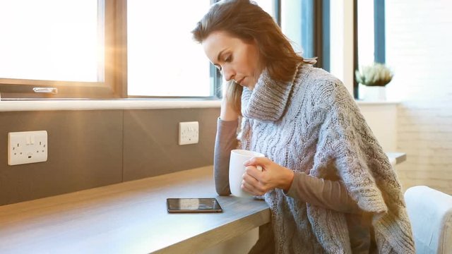 Beautiful young woman enjoying a hot drink in a coffee shop while relaxing and using a tablet computer