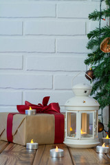 Christmas Decorations. Gift box, lamp with candle, cone on wooden table against brick background
