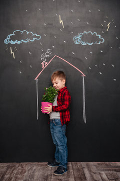 Kid standing in house on chalkboard holding flower and smelling