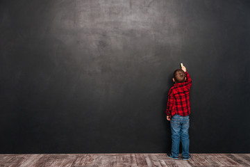 Little child standing near blackboard and drawing on it