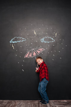 Cheerful kid holding umbrella on chalkboard with drawings of rain
