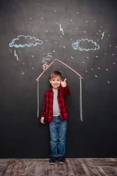 Kid in house over chalkboard background making thumbs up gesture