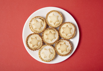 Aerial view of a plate full of freshly baked mince pies on a bright red background