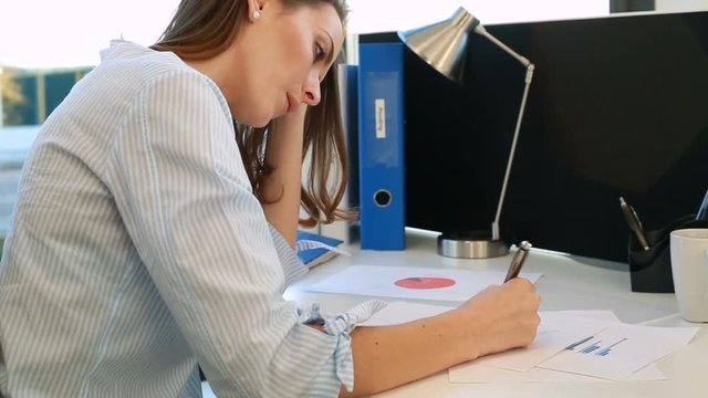 Young business woman working at her desk going over charts and graphs expressing concern and stress