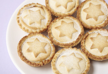 A plate full of freshly baked mince pies on a pastel purple background