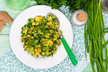 Potato salad on a white plate with fresh herbs, a top view