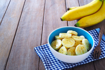 Top view of a bowl of sliced ripe banana on wooden background.