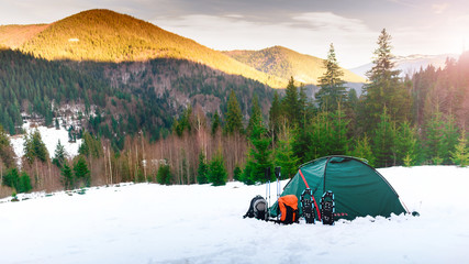 Tent. backpacks. trekking poles, snowshoes on snow in the mounta