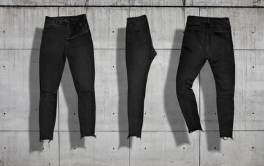 Set of different shots of skinny torn black jeans from the front, the back and folded in half on concrete industrial background