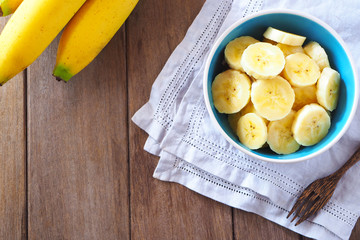 Top view of a bowl of sliced ripe banana on wooden background.
