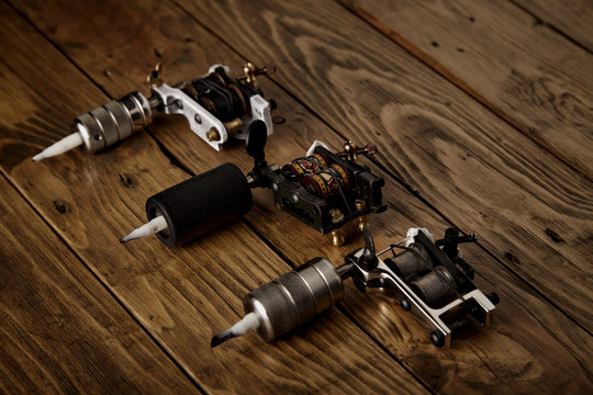 Three different handmade electric traditional tattoo guns arranged on a brown wooden table