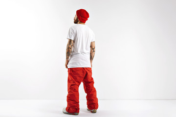 Back shot of a young guy wearing red snowboard pants, large plain white cotton t-shirt and red beanie isolated on white