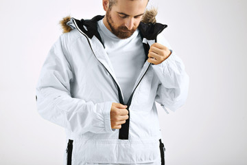 Serious attractive young man zipping up his snowboarding white jacket over unlabeled white t-shirt isolated on white © BublikHaus