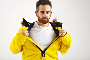 Sexy bearded young man showing plain white t-shirt under his bright yellow snowboarding jacket isolated on white