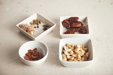 Various nuts, dried fruits and spices beautifully arranged in small white bowls of different shapes on rough white surface