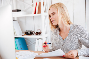 Casual young businesswoman making notes while looking at computer monitor