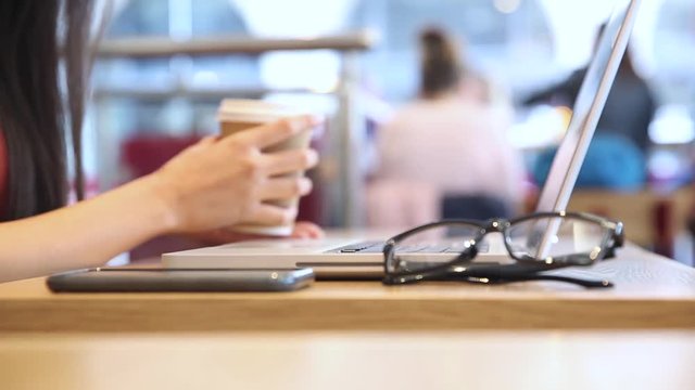 Woman typing on computer and drinking coffee in a cafe
