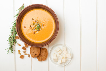 Pumpkin soup with bread crouton on white wooden table.