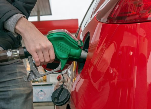 Man Is Pumping Gas In Red Car In Fuel Station.