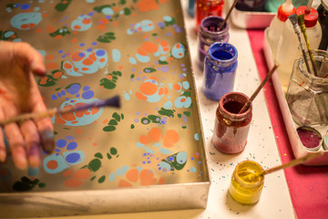 Traditional Turkish art Ebru in process. Woman hand sprinkling paint over water and colourful paint bottles standing next to the ebru tray