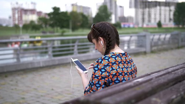 young woman sitting on a bench in the park and listening to music
