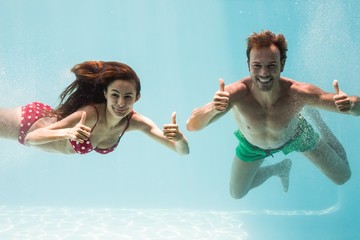 Smiling couple showing thumbs up while swimming
