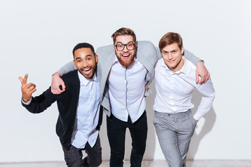 Three cheerful young men standing and smiling together