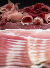 Ham mix. jambon. Traditional Italian and Spanish salting, smoking, dry-cured dish - jamon Serrano and prosciutto crudo sliced with herbs and tomatos on dark stone background. Copy space. Closeup. 